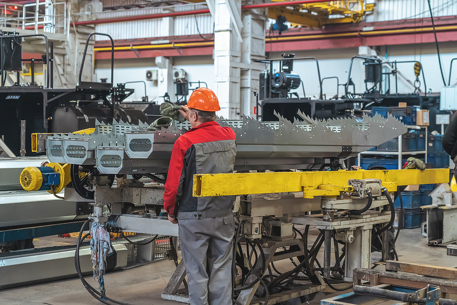 Worker in process of assembling components for the production of combines or tractors at industrial manufacturing production line.