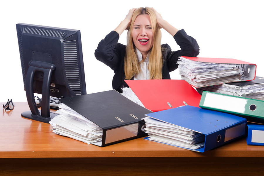 person at desk looking frustrated by pile of overflowing binders. ERP