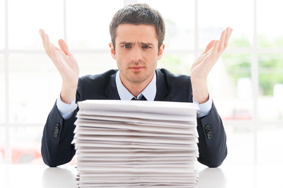 person throwing up his hands in front of a stack of papers on the desk, document management